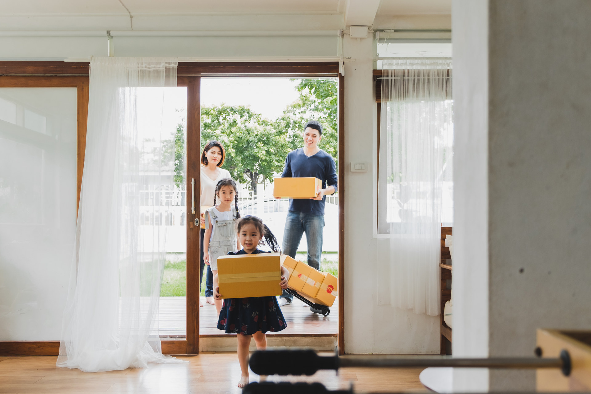 Family entering a bright room carrying cardboard boxes.